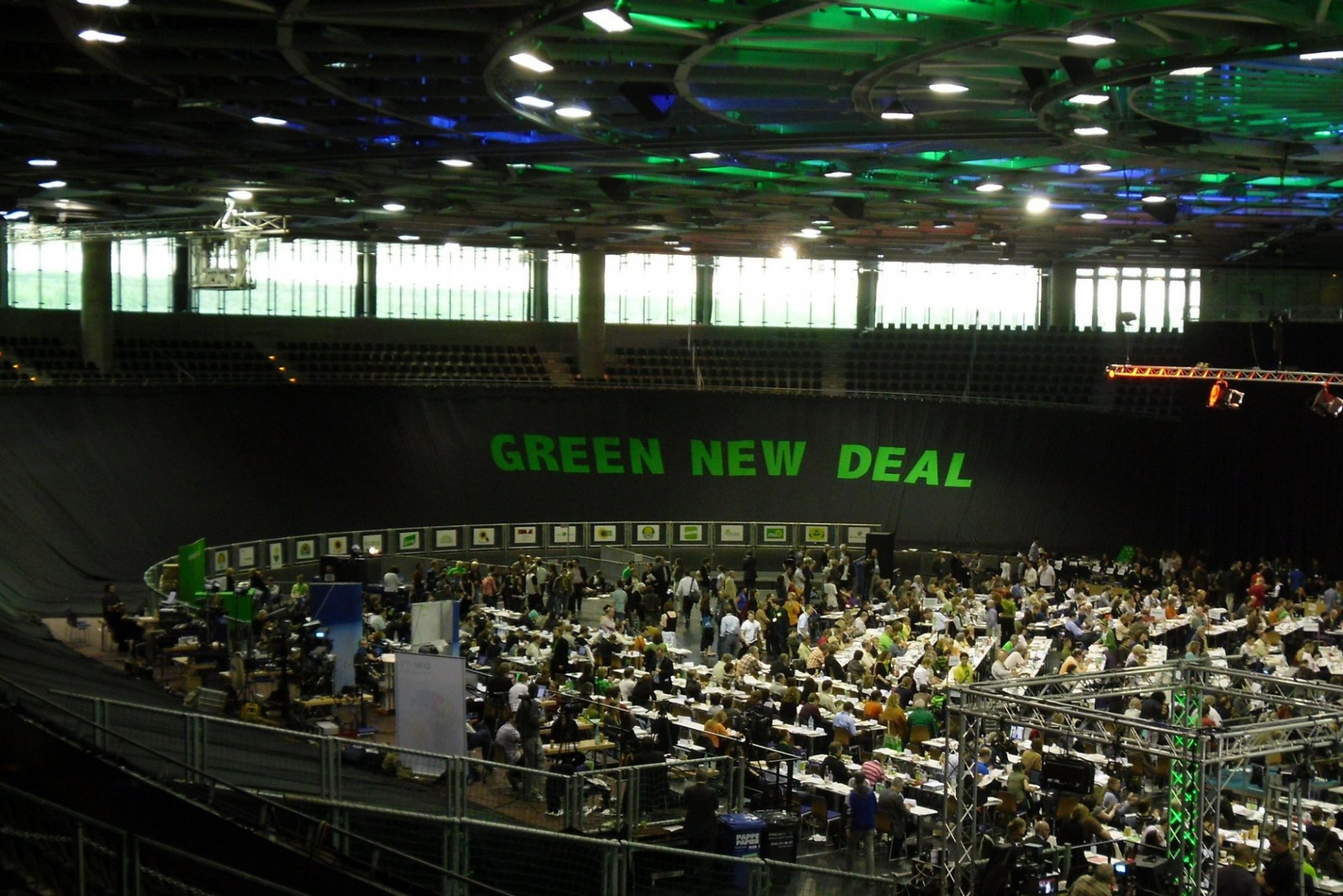 A conference center with people gathering in the foreground and a Green New Deal sign in the background.  